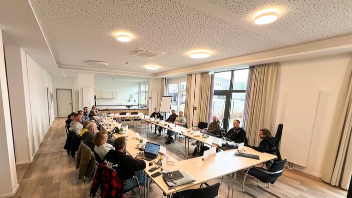 Mehrere Personen sitzen an Tischen in einem Seminarraum